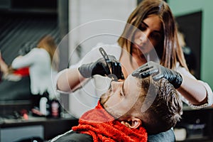 Girl hairdresser shaves his beard with a man razor