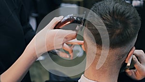 Girl the hairdresser shears the guy with a clipper. Guy speaks on the phone