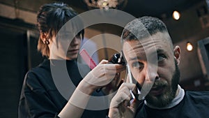 Girl the hairdresser shears the guy with a clipper. Guy speaks on the phone