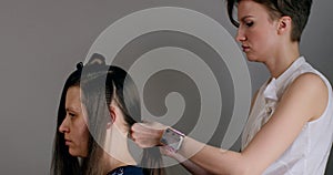 Girl hairdresser-stylist in white shirt with short stylish hairstyle combs her hair and makes festive hairstyle to sitting girl.