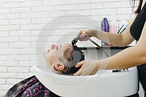 A girl hairdresser washes the hair of a client in a beauty salon.