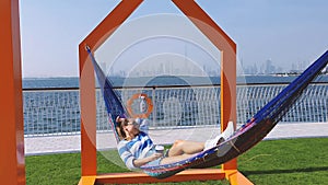 The girl in the hammock on the beach near Dubai city on the background. Woman with coffee at a pier at UAE.