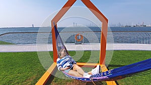 The girl in the hammock on the beach near Dubai city on the background. Woman with coffee at a pier at UAE.