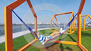 The girl in the hammock on the beach near Dubai city on the background. Woman with coffee at a pier at UAE.