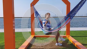 The girl in the hammock on the beach near Dubai city on the background. Woman with coffee at a pier at UAE.