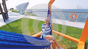 The girl in the hammock on the beach near Dubai city on the background. Woman with coffee at a pier at UAE.