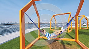 The girl in the hammock on the beach near Dubai city on the background. Woman with coffee at a pier at UAE.