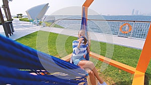 The girl in the hammock on the beach near Dubai city on the background. Woman with coffee at a pier at UAE.