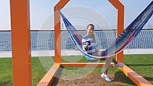 The girl in the hammock on the beach near Dubai city on the background. Woman with coffee at a pier at UAE.