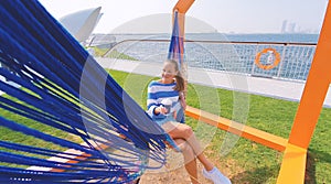 The girl in the hammock on the beach near Dubai city on the background. Woman with coffee at a pier at UAE.