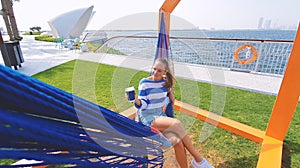 The girl in the hammock on the beach near Dubai city on the background. Woman with coffee at a pier at UAE.