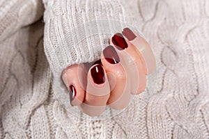 Girl hand with brown nails polish color on white woolen sweater background