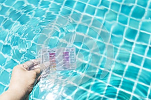 Girl hand dipping water testing test kit in clear swimming pool water to test pH and chlorine