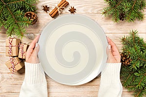 Girl hand hold Top view. Empty white plate on wooden background with christmas decoration. New Year concept