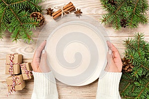 Girl hand hold Top view. Empty white plate on wooden background with christmas decoration. New Year concept