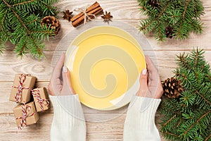 Girl hand hold Top view. Empty yellow plate on wooden background with christmas decoration. New Year concept