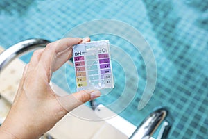 Girl hand holding mini water testing test kit over blurred swimming pool background