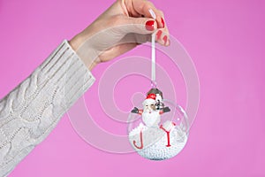 Girl hand holding ornament ball with snow isolated on pink background in studio