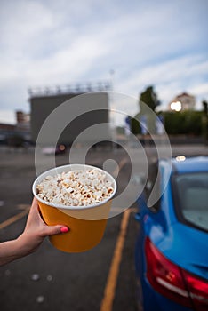 Girl hand holding popcorn bucket on autocinema parking