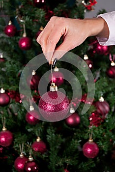 Girl hand holding red decoration for Christmas tree and blurry tree in background