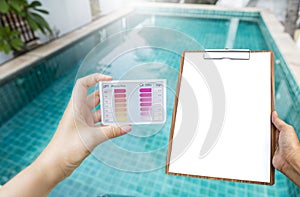 Girl hand holding water testing test kit with blank report sheet in girl hand over swimming pool background