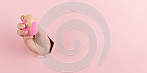 Girl hand holds a beauty blender in foundation, concealer from a hole in a pink background. Makeup artist concept, copy space