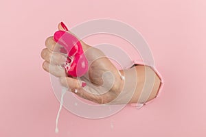 Girl hand holds a beauty blender for makeup from a hole in a pink background, copy space. Sponge in soapy foam, how to clean