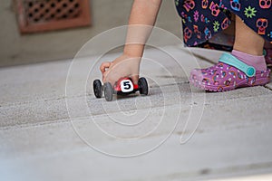 Girl hand playing with a red toy car on an outdoor floor