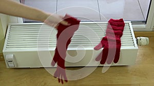 Girl hand put red woolen gloves on radiator at home.