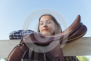 Girl With Hand Resting On The Wooden Fence A Leather Saddle Hanging On The Fence