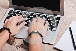 A girl in handcuffs is sitting at a laptop. The concept of censorship or restriction of freedom of speech or punishment for photo