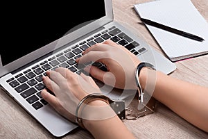 A girl in handcuffs is sitting at a laptop. The concept of restricting freedom of speech or punishing the disclosure of