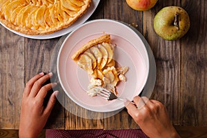 Girl hands eating a portion of apple pie tart on rustic wooden t