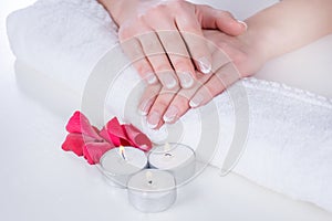 Girl hands with french manicure modern style on towel with red rose petals and candle in beauty salon