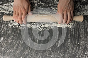 Girl hands keep rolling pin with flour on dark black table, baking background, top view, copy space for your text, meru, recipe