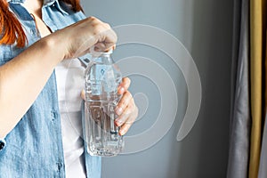 Girl hands open a bottle of water in room. Thirst Concept