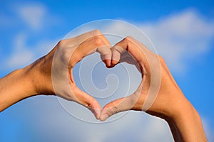 Girl hands in shape of love heart on blue sky