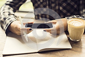 Girl hands with smartphone, blank diary with pen and coffee