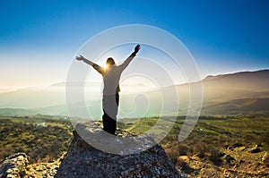 Girl with hands up in the mountains against sun