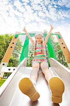 Girl with hands up sits on playground chute