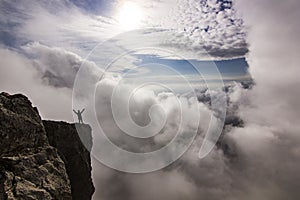 Girl with hands up standing on a cliff in clouds