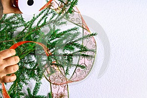 A girl is hanging a Christmas ribbon from the organza on a Christmas tree on a white background.