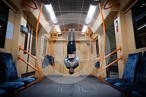 Girl hanging by feet upside down in the subway carriage and using smartphone. Concept of overusing social networks and