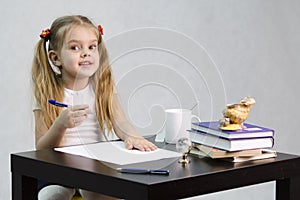 The girl happily looks in the frame, sitting at the table in the image of the writer