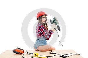 girl in hardhat posing with grind tool on wooden table with tools,