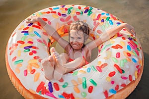 Girl has fun on big donut inflatable ring on lake on hot summer day, happy summertime, countryside