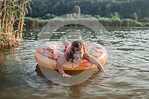 Girl has fun on big donut inflatable ring on lake on hot summer day, happy summertime, countryside