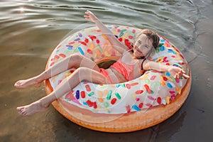 Girl has fun on big donut inflatable ring on lake on hot summer day, happy summertime, countryside