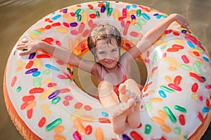 Girl has fun on big donut inflatable ring on lake on hot summer day, happy summertime, countryside