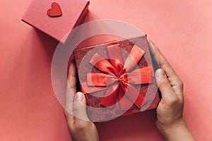 The girl has received a gift in a beautiful red box with a ribbon and is going to open it.